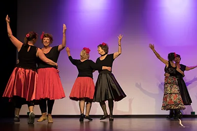 Women wearing colourful dresses on stage twirling around each other