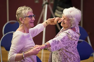 Two elderly women smiling and dancing together