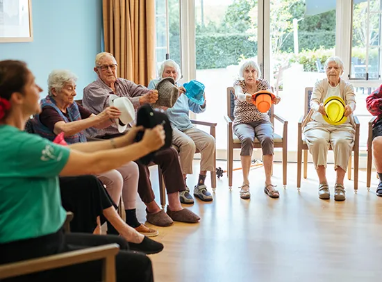 Elderly group sitting in chairs learning a seated dance with hats