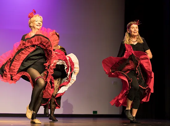 Two older women on stage dancing with big flowing skirts