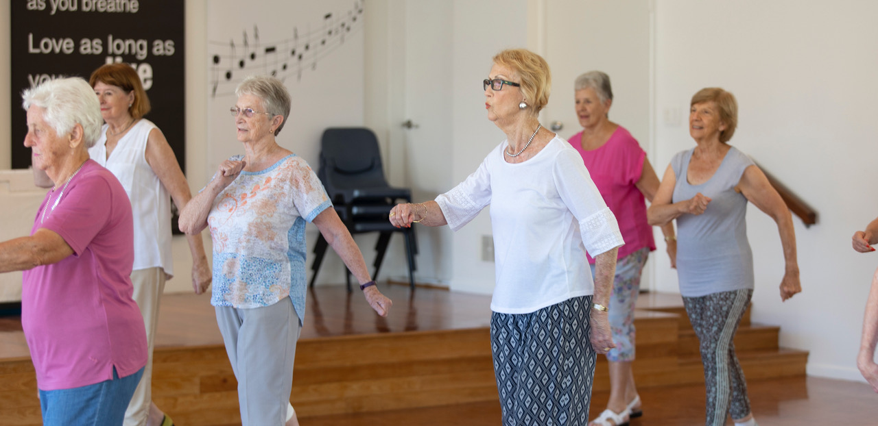 Older people participating in a standing dance class in person.